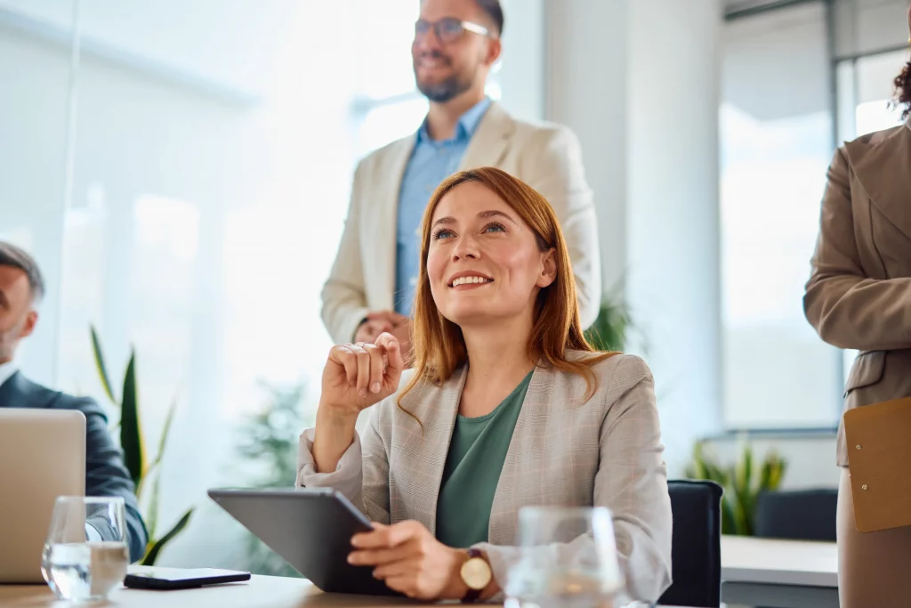 Lächelne, rothaarige Frau schaut während eines Meetings mit Kollegen nach oben