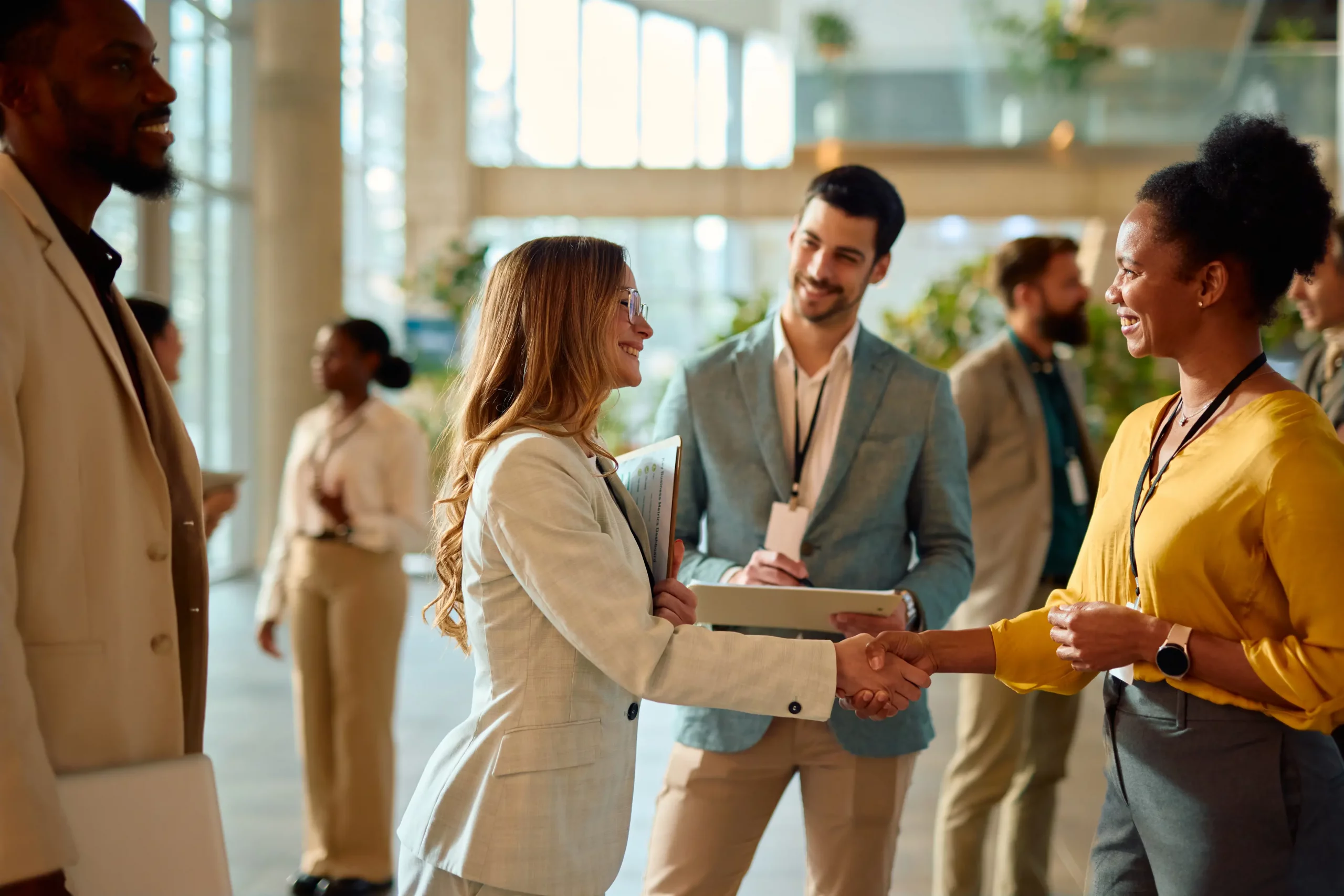 Zwei Frauen begrueßen sich mit einem Handschlag vor anderen Kollegen in einer Empfangshalle