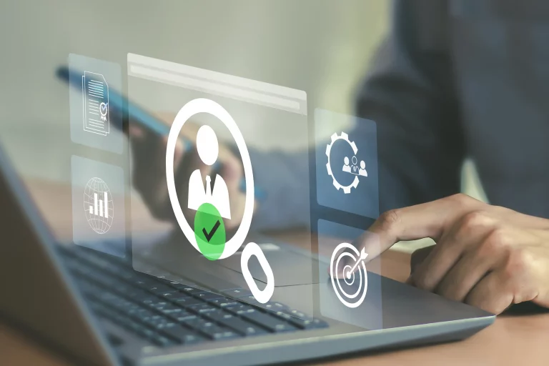 Nahaufnahme einer Hand vor einem Laptop mit einem Smartphones und einer Projektion